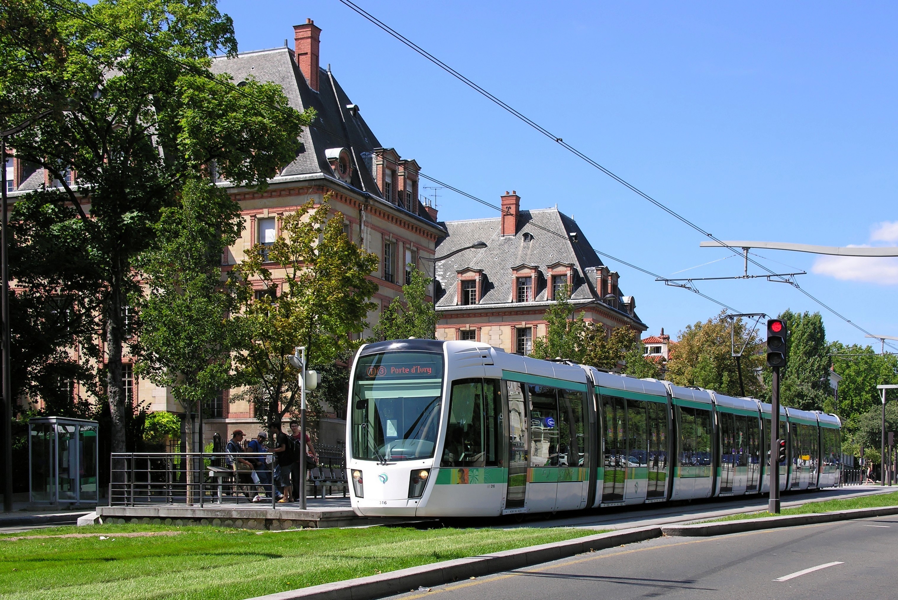 Paris T3 tram running on grass-covered tracks alongside tree-lined boulevard